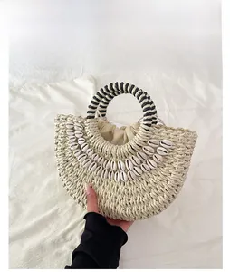 Detail of semi-circular straw bag with shell decor and black-white braided handle