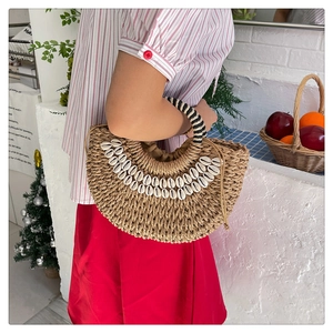 Close-up of handmade straw handbag with white shell decor and striped handle