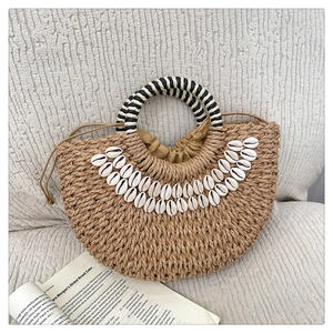 Detail of a semi-circular straw bag with shell accents and striped handles on white texture
