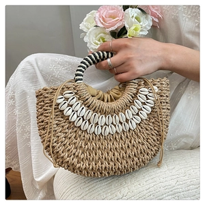 Detail of handmade semi-circle straw bag featuring natural shells and striped handles