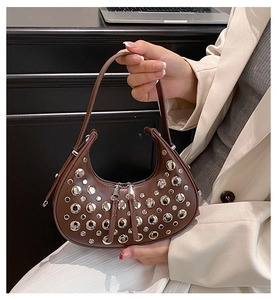 Detail of a brown leather crescent shoulder bag featuring dense silver stud embellishments
