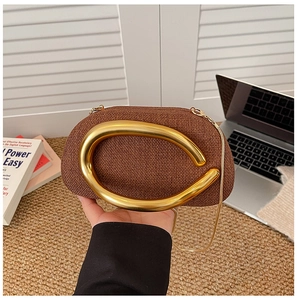 Detail of a brown woven clutch featuring a large gold C-handle and fine chain strap