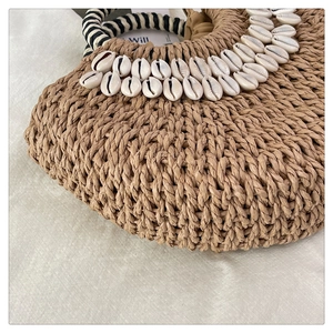 Detail of straw woven handbag with shell embellishments and striped handles