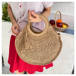 Detail of round woven straw bag featuring decorative long tassels and circular handles