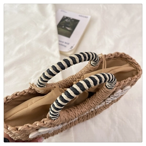 Detailed close-up of handmade shell straw bag with striped handles and drawstring liner