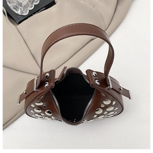 Detail shot of brown leather dumpling bag with silver rivets on textured beige fabric