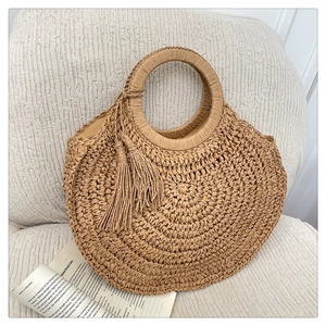 Detail of round woven straw bag with tassel fringe resting on a textured white fabric