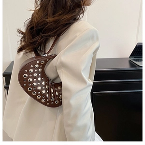 Detail of a brown crescent shoulder bag with silver studs worn with a white blazer
