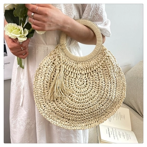 Detailed close-up of a round straw woven handbag featuring natural tassel decorations