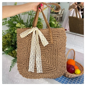 Detail of hand-woven raffia tote bag featuring a large white lace bow and brown leather straps