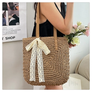 Detail of raffia woven tote bag featuring a large white lace bow and long shoulder straps