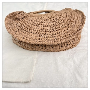 Detailed close-up of straw woven handbag with decorative side tassels and circular handle