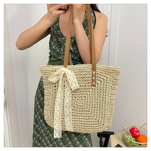 Detail of raffia woven tote with white lace bow and brown handles for summer beach