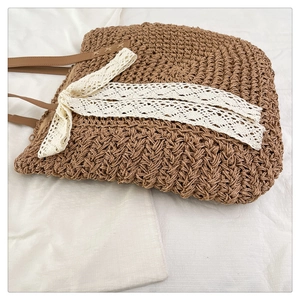 Detail of raffia woven tote bag featuring white lace ribbon and brown leather handles