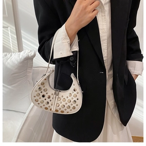 Close-up of white crescent bag with silver stud details worn with a black blazer