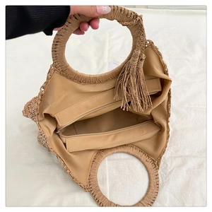 Detail view of the round straw handbag showing inner zippered lining and tassel ornament