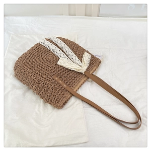 Detail of raffia straw woven tote bag featuring a delicate white lace bow and leather strap