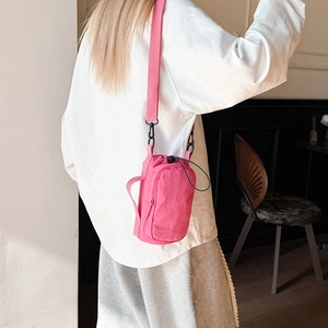 Magenta waterproof nylon crossbody bag with wide strap worn by a model in a cafe