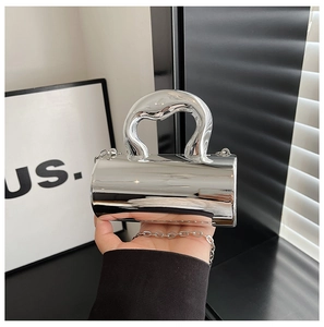 Detail of silver cylindrical handbag featuring a unique melting fluid handle and chain