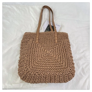 Close-up of raffia woven tote featuring brown leather handles and cross-stitch detail