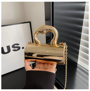 Macro view of a gold cylindrical evening clutch with mirrored finish and metal chain
