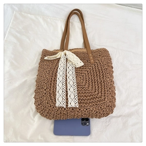 Detail of raffia woven tote with lace bow and leather handles next to a phone for size