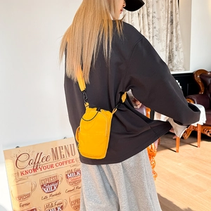 Detail of yellow nylon crossbody bag with fabric strap and black metal hook hardware