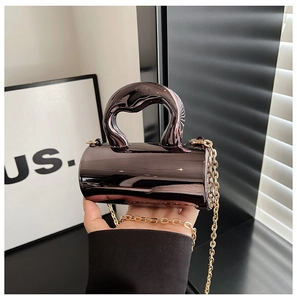 Detail of a dark brown glossy cylindrical mini bag with a twist handle and gold chain