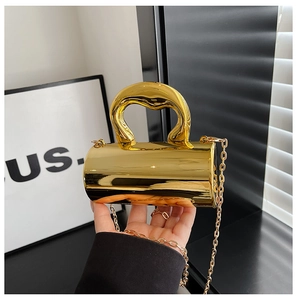 Macro shot of mirror-finish gold cylindrical handbag with streamlined handle and chain strap