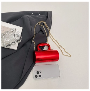 Detailed view of mini red cylindrical bag with gold chain next to a smartphone