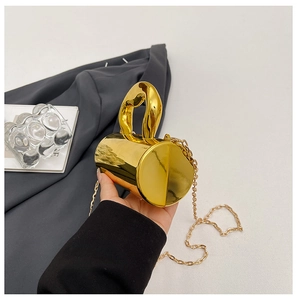 Close-up of golden cylindrical evening bag with metal handle and detachable chain strap