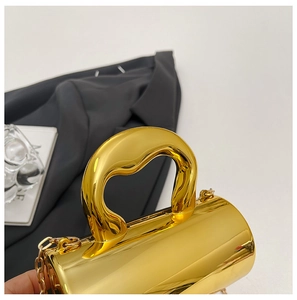 Macro view of golden cylindrical evening bag with mirror finish and metal chain strap