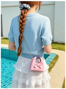 Rear view of a girl wearing a pink mini bow crossbody bag by a poolside