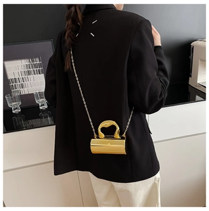 Golden cylindrical acrylic evening bag with chain strap held by a model in a minimalist room