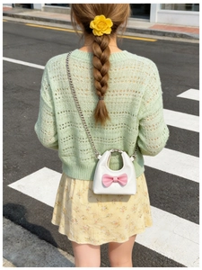 Close-up of white mini girl's crossbody bag with pink bow and silver chain strap