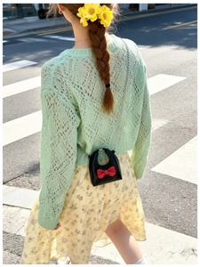 Outdoor shot of a girl wearing a black shiny mini bag with a red bow and chain strap