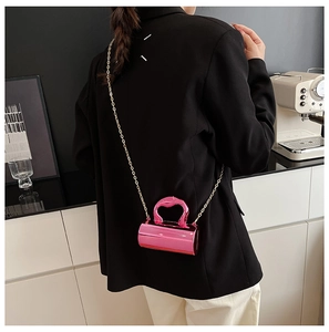 Close-up of pink mini cylinder bag with heart handle and gold chain on black blazer
