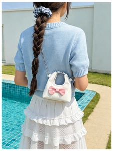 Detail of a mini white leather girl bag with pink bow and silver chain strap