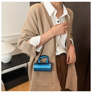 Close-up of a mini cylindrical blue mirror handbag with a gold chain strap on a model