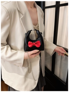 Close-up of mini black crossbody bag with red bow and silver chain strap on model