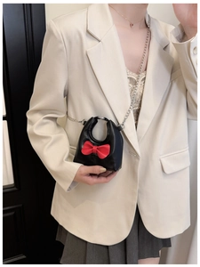 Mini black crossbody bag with red bow and silver chain strap shown on a young girl