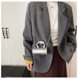 Close-up of a mini silver metallic cylindrical evening bag with metal handle and chain strap