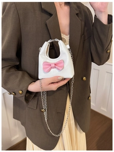 Detail of a white mini leather bag with a pink bow and silver chain strap