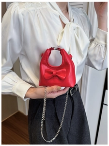 Detail of red mini bow purse with silver chain strap on a white silk shirt
