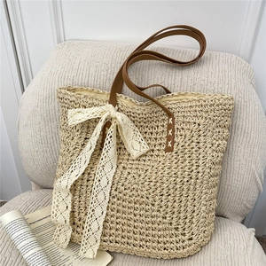 Large beige raffia crochet beach bag with lace bow and brown leather handles on a sofa