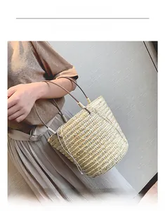 Detail view of the hand-woven straw bucket bag with dark brown leather handles on a model