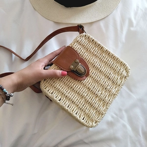 Detail view of woven straw beach bag featuring brown leather flap and retro metal clasp