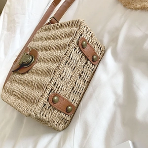 Detail of square straw beach bag with brown leather trim and retro metal clasp lock