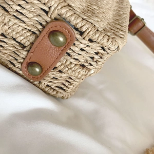 Close-up of brown leather strap attachment and metal rivets on a woven straw bag