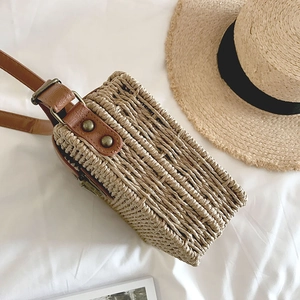 Detail of handwoven straw crossbody bag with brown leather strap and metal rivets